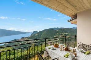 A balcony with a table set for tea, overlooking a lake and mountains.