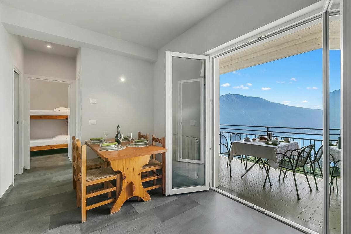 Une chambre moderne avec une table à manger en bois, des chaises, un lit et un balcon offrant une vue sur les montagnes.