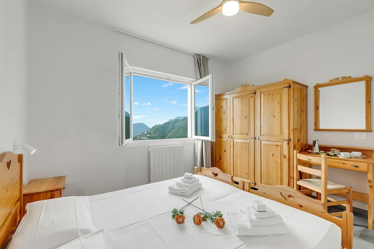 Une chambre d’hôtel avec un lit, une armoire en bois, un bureau et une fenêtre donnant sur la montagne.