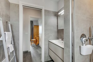 Ein modernes Badezimmer mit grauen Fliesen, einem weißen Waschbecken und einer Duschkabine.