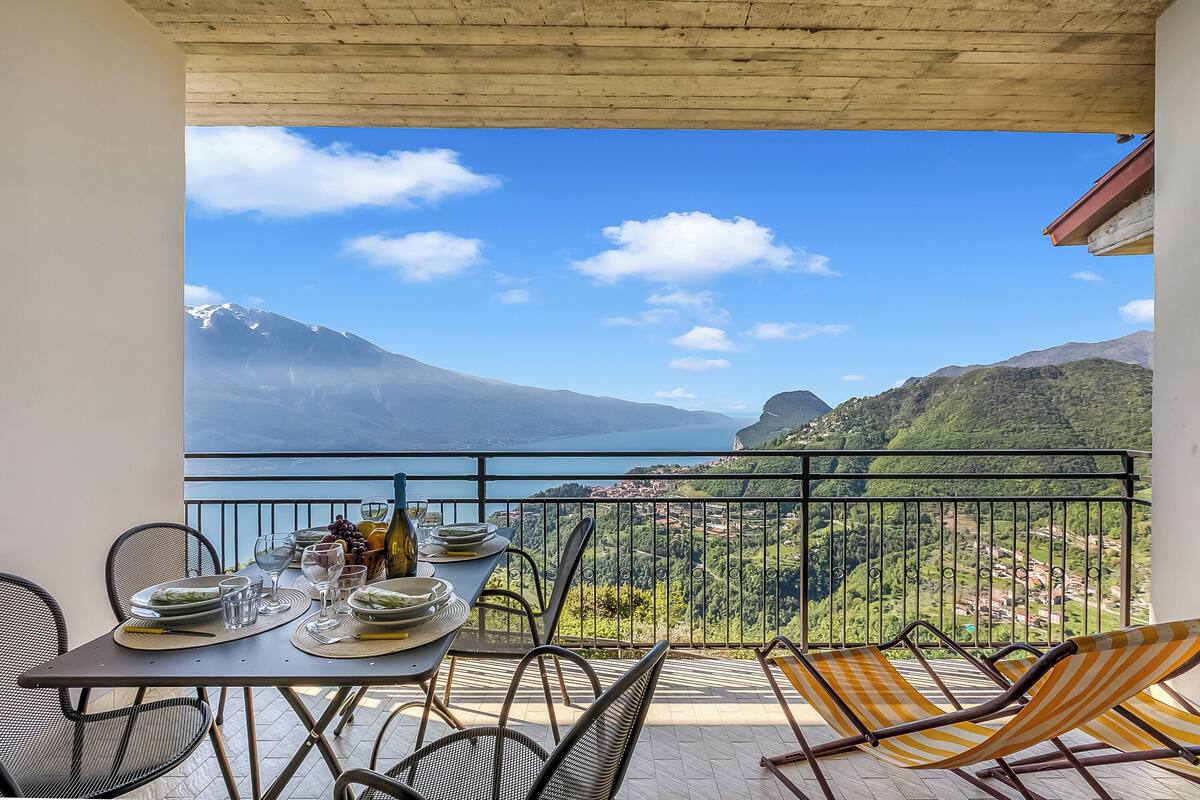 Varanda com mesa posta para refeições, cadeiras e vista para uma paisagem montanhosa.