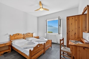 A bedroom with a wooden bed, a desk, and a view of a mountain through an open window.