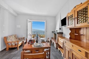 A dining area with a wooden table, chairs, a sofa, and a view through an open door.