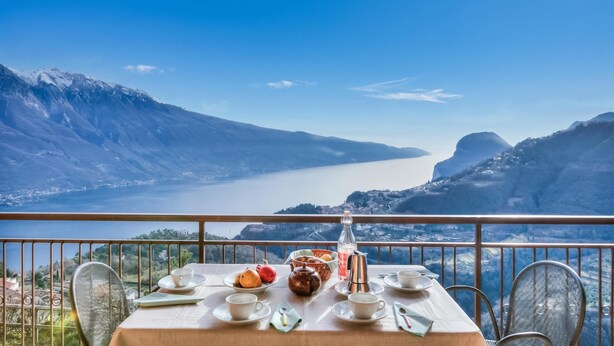 Une table dressée avec des tasses, des soucoupes, une théière et une bouteille, donnant sur un paysage montagneux avec un lac.