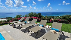 Ein Poolbereich mit Liegestühlen und Blick auf den Ozean.