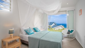 Ein Schlafzimmer mit Bett, Nachttisch, Stuhl und Meerblick.