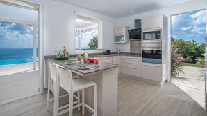 Eine moderne Küche mit einer großen Kochinsel, weißen Barhocker und Meerblick.