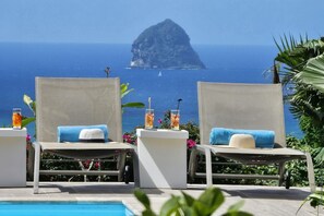 Two lounge chairs with towels, a pool, and a view of the ocean with a prominent rock formation. - Carpe Diem (Sainte-Luce)