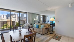 A modern living room with a city view, a dining area, and a large window. - Deluxe Ocean and City View Waikiki Banyan Condo, Free Parking & Wi-Fi (Honolulu)