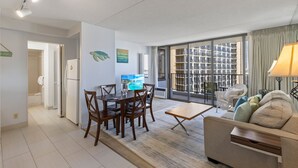A modern living room with a dining area, a sofa, and a large window with a view of buildings. - Deluxe Ocean and City View Waikiki Banyan Condo, Free Parking & Wi-Fi (Honolulu)