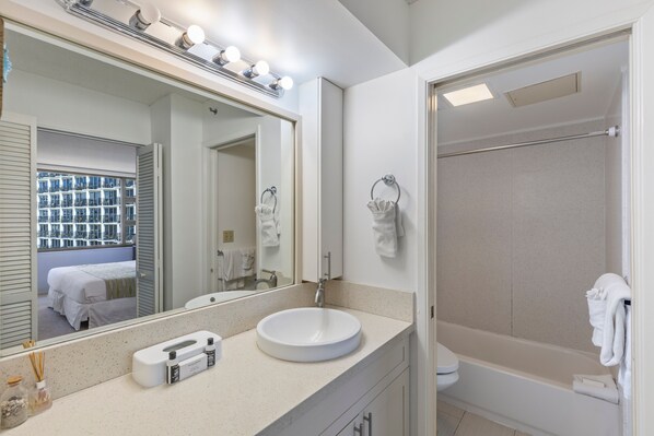 A bathroom with a round sink, a large mirror with lights, a shower, and a toilet. - Deluxe Ocean and City View Waikiki Banyan Condo, Free Parking & Wi-Fi (Honolulu)