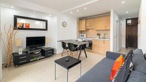 A modern living room with a flat-screen TV, a dining table with chairs, and a sofa with a throw pillow. - GO2TENERIFE Apart'Lotus Pool + beach 400m (Arona)