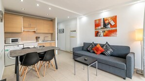 A modern kitchen with wooden cabinets, a dining table with chairs, and a grey sofa with decorative pillows. - GO2TENERIFE Apart'Lotus Pool + beach 400m (Arona)