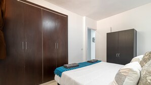 A bedroom with a large wardrobe, a bed with a quilted cover, and a blue throw blanket. - GO2TENERIFE Apart'Lotus Pool + beach 400m (Arona)
