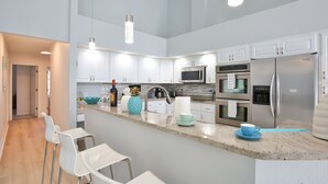 Una cocina moderna con armarios blancos, electrodomésticos de acero inoxidable y una zona de bar con sillas blancas.