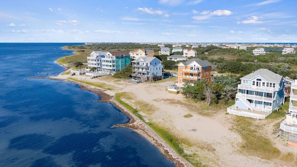 Zona residencial costera con propiedades frente al mar, que incluyen edificios de varios pisos, algunos con balcones, y una playa de arena junto al océano.