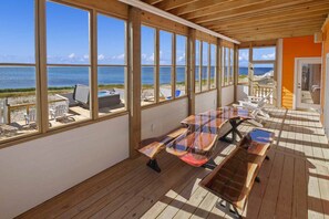 Un espacio de estar al aire libre con techo y vistas al océano, suelo de madera y una mesa larga con sillas.