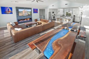 A modern living room with a large sectional sofa, a fireplace, and a unique wooden coffee table. - Luxury Soundfront w/ Pool, Hot Tub, Elevator, Watersports Access, Media Room (Avon)