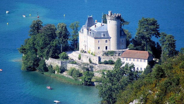 Un château doté d’une tour, entouré d’eau et de verdure.