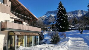 Un bâtiment moderne doté d’un balcon, de grandes fenêtres et surplombant un paysage enneigé avec des montagnes en arrière-plan.