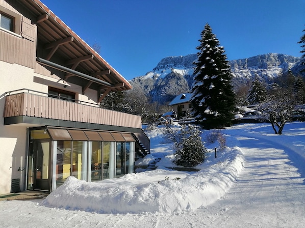 A modern building with a balcony, large windows, and a snow-covered landscape with mountains in the background.
