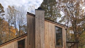 A wooden cabin with a sloped roof, large windows, and a chimney.