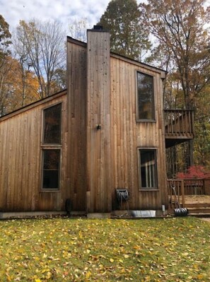 Una cabaña de madera con techo inclinado, ventanas grandes y una chimenea.