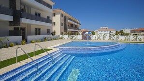 Una piscina con escalones de acceso, rodeada de edificios modernos con balcones.
