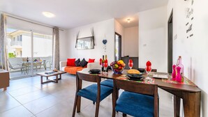 Una sala de estar moderna con comedor, que incluye un sofá, una mesa de centro y una mesa de comedor dispuesta con fruteros, copas de vino y botellas.
