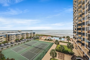 Un hotel de varios pisos con cancha de tenis, piscina y vista al mar.