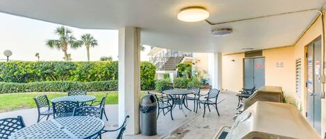 An outdoor patio area with round tables and chairs, a barbecue grill, and a trash can.