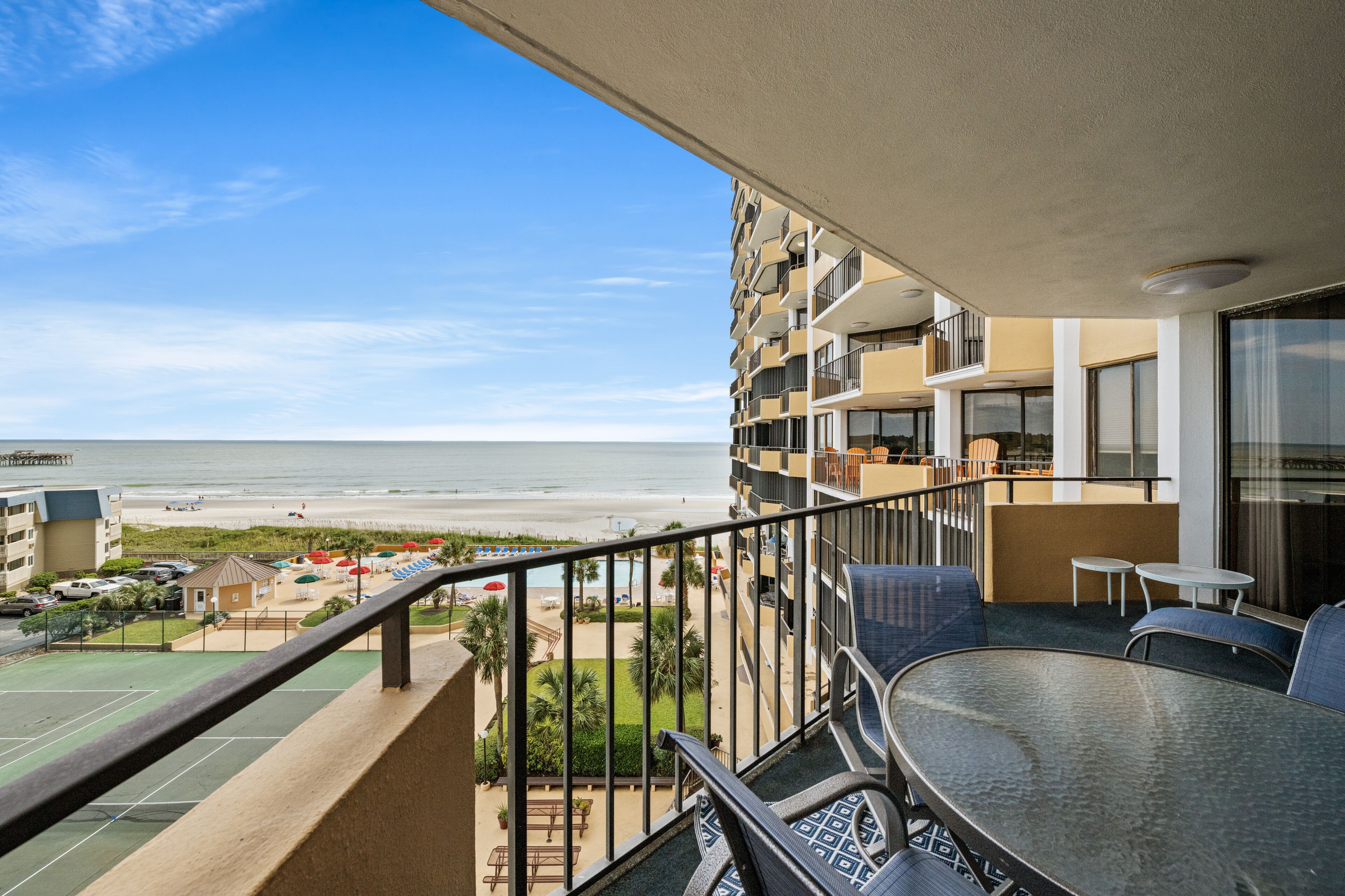 A balcony with a view of the beach and ocean, a pool, and outdoor seating.