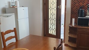 A compact kitchen with a wooden dining table, chairs, a refrigerator, and a coffee maker. - Charming village house in the heart of the Luberon (Pierrevert)