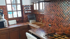 A kitchen with wooden cabinets, a gas stove, a sink, and a window with a view of the outside. - Charming village house in the heart of the Luberon (Pierrevert)