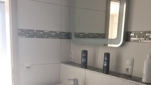 A bathroom with a white sink, dark cabinetry, a mirror, and toiletries on the countertop. - Holiday apartment North (WA325) (Wackersdorf)
