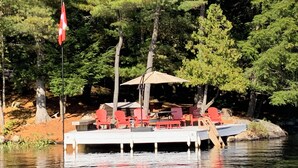 Un bateau amarré, avec des chaises rouges et une table, entouré d’arbres et d’un drapeau.