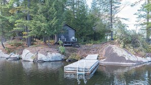 Une cabane avec un quai s’avançant dans un lac, entourée d’une forêt dense.