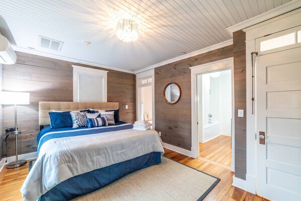 Un dormitorio con una cama grande, paredes de madera, una araña de cristal y una puerta que da a otra habitación.