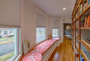 Una habitación con un banco empotrado junto a las ventanas, una estantería de madera y un pasillo que conduce a otra habitación.