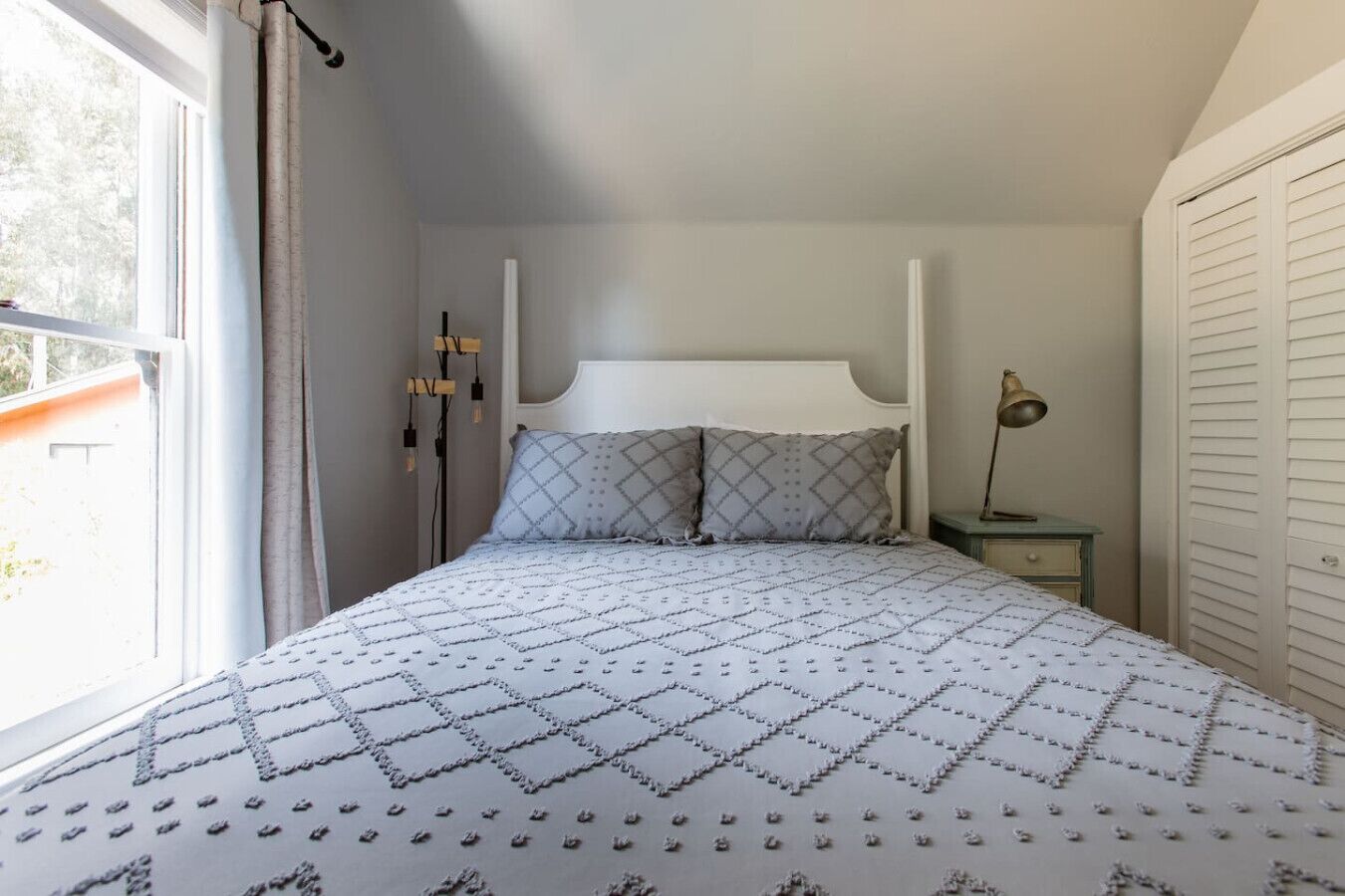 A bedroom with a bed, a nightstand, a lamp, and a window with curtains.