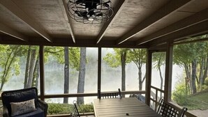 A covered outdoor seating area with a table and chairs, overlooking a forested area. - Fairway Villa 305 at Rumbling Bald (Lake Lure)