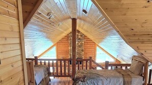 Een gezellig slaapkamer op zolder met houten wanden en schuine plafonds, met twee bedden en een klein krukje.