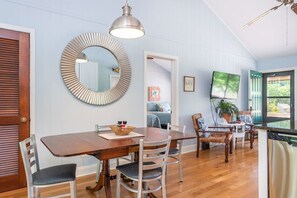 A dining area with a wooden table, white chairs, a large mirror, and a ceiling fan.