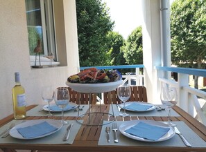 Mesa para dos personas dispuesta con platos, cubiertos y copas de vino. Hay un plato de mariscos sobre la mesa y se ve una botella de vino. El ambiente es al aire libre con vista a árboles y una barandilla.
