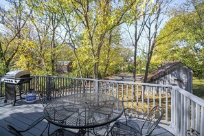 Une terrasse avec une table et des chaises en métal, un barbecue et un abri de jardin.