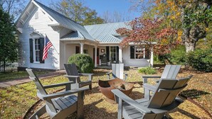 A white house with a porch, outdoor seating, and a fire pit.