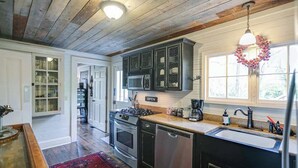 A kitchen with wooden ceiling, stainless steel appliances, and a red rug.