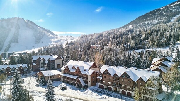 A lodge with multiple buildings, a ski slope in the background, and snow-covered trees. - 4 BD/3BA Redstone Chalets E (Rossland)