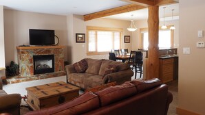 A living room with a stone fireplace, leather sofa, wooden coffee table, and a television on a mantel. - 4 BD/3BA Redstone Chalets E (Rossland)