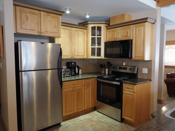A compact kitchen with wooden cabinets, stainless steel appliances, and a tiled backsplash. - 4 BD/3BA Redstone Chalets E (Rossland)